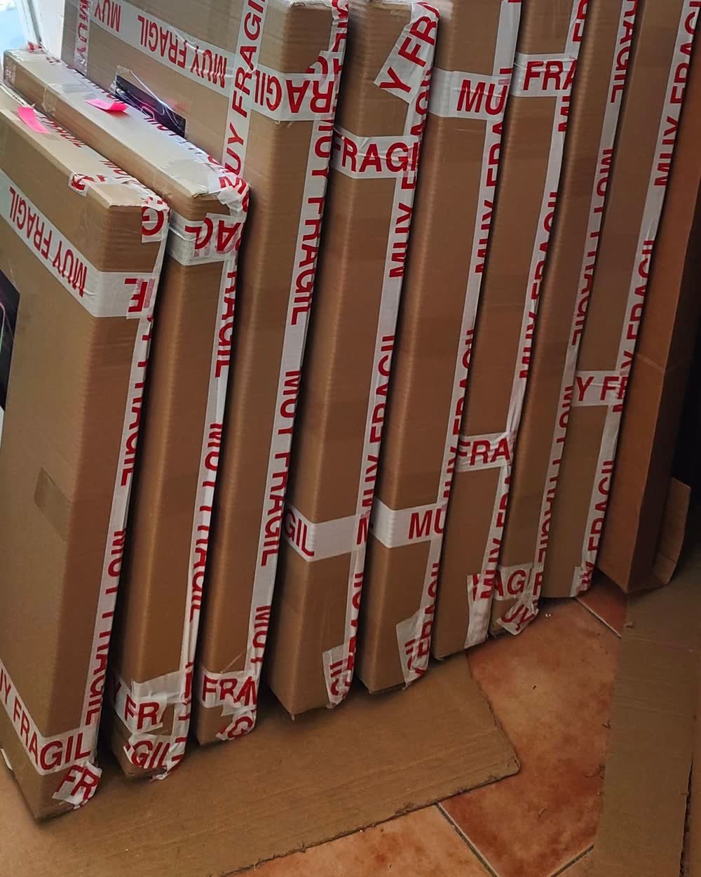 Diez cajas grandes con cuadros de resina epoxi embalados y precintados con cinta de muy fragil, apoyadas contra la pared del taller listas para el transportista